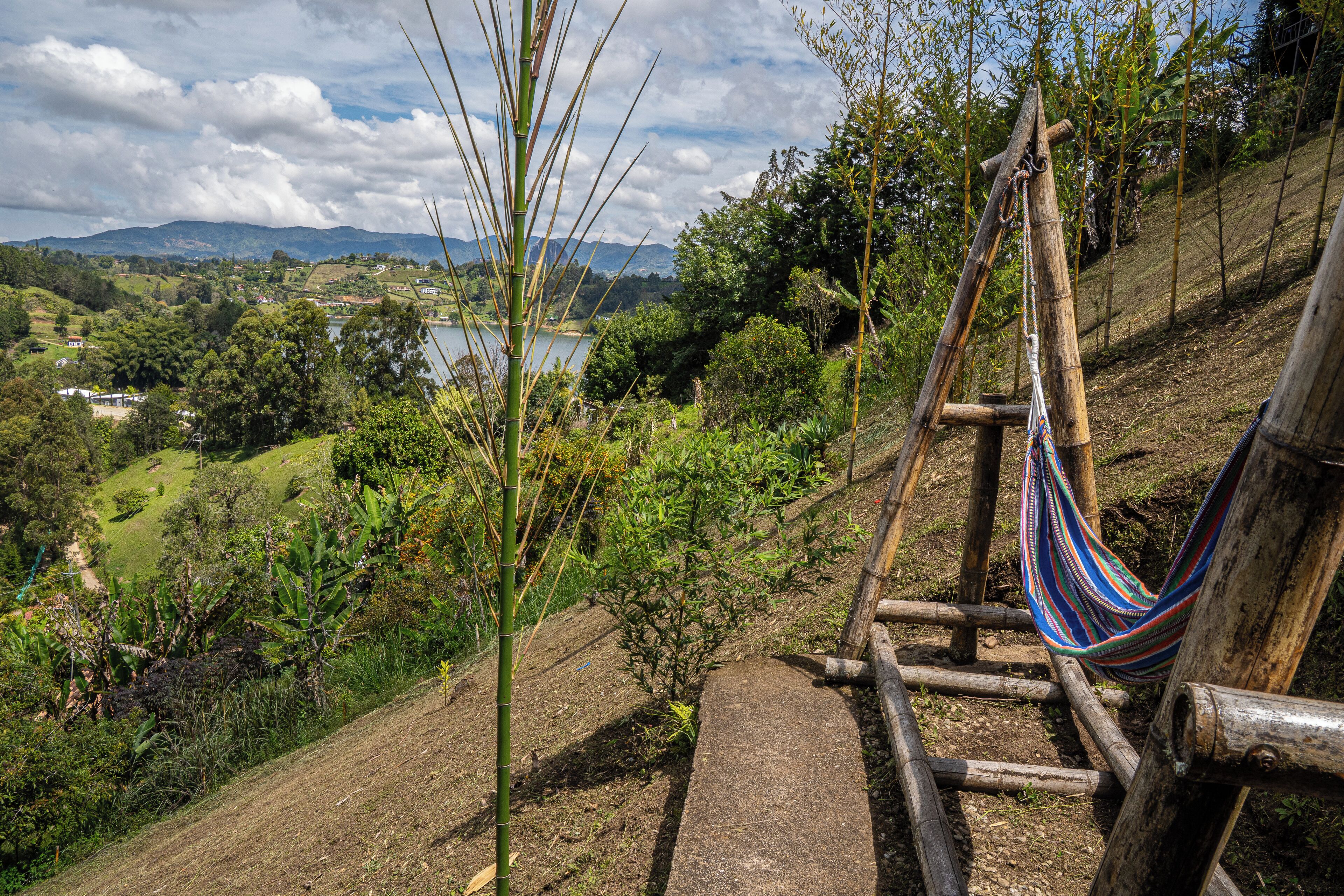 A hammock tied to a wooden structure overlooking a lush landscape with a body of water and distant mountains.