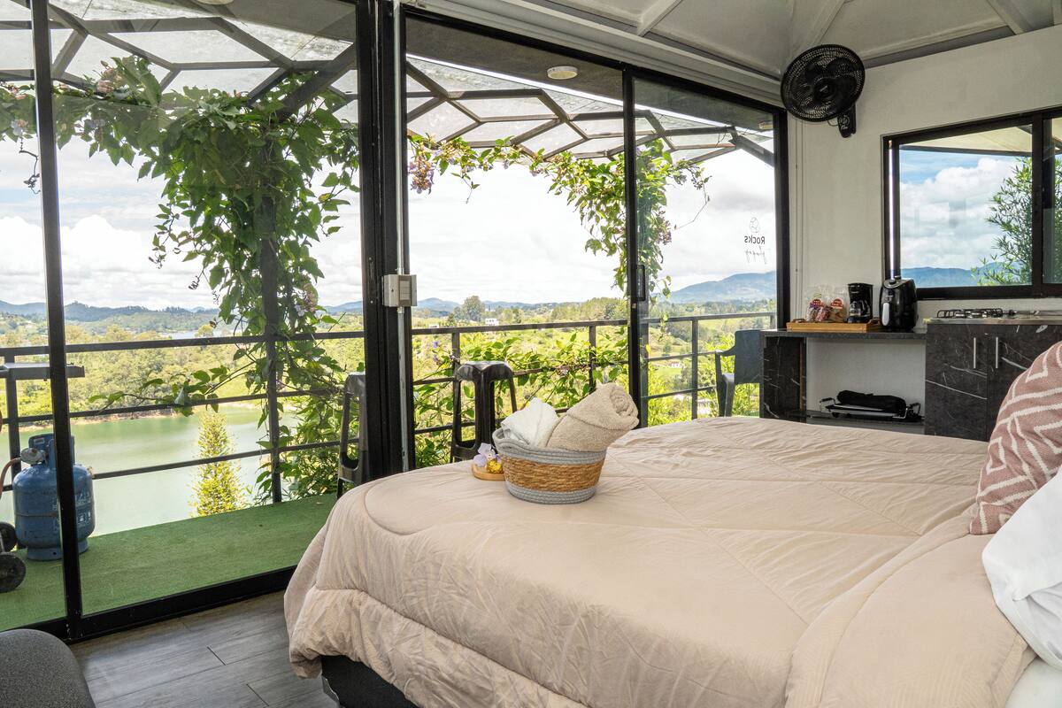 A bedroom with a large bed, a view of a lake, and a balcony with a view of the surrounding landscape.