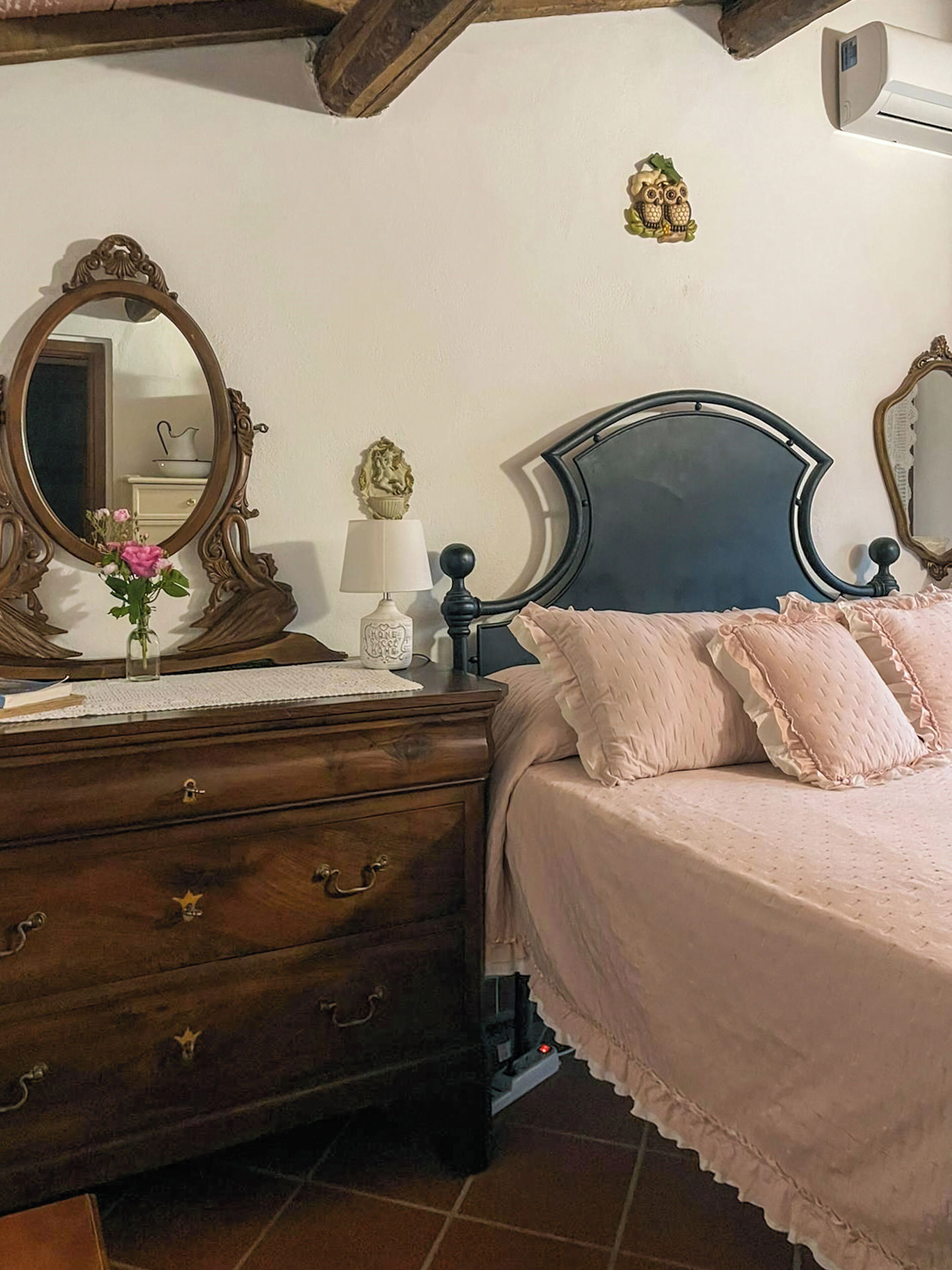 Una camera da letto con un comò in legno, un letto con testiera, uno specchio e un condizionatore d'aria a parete.