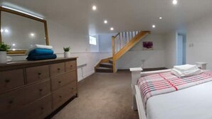 Un dormitorio con cama, cómoda, espejo y una escalera que sube a otra habitación.