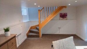 Un interior moderno con una escalera de madera, una planta pequeña y una lámpara fijada a la pared.