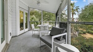 Un balcon abrité, doté d’un ventilateur de plafond, de meubles blancs et offrant une vue sur la verdure et les bâtiments.