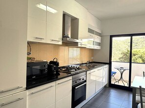 A modern kitchen with white cabinets, a black stove, and a window overlooking a balcony. - Casa Linda by Sesimbra Sun Sea (Sesimbra)