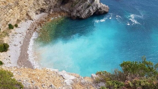 Un paisaje costero con un acantilado rocoso y un mar azul cristalino.