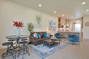 A modern living room with a brown leather sofa, a coffee table, and a dining area with a round table and stools. - Luxury New Build in Western District OKC for a large family (Oklahoma City)