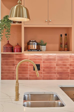 A kitchen with a modern design, featuring a stainless steel sink, a gold faucet, and a pendant light above the counter. - Luxury New Build in Western District OKC for a large family (Oklahoma City)