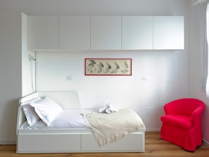 A bedroom with a bed, a red chair, and a wall-mounted shelf with a framed picture. - Casa Sabotino Modern Functional and Cozy (Bologna)