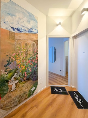 A hallway with a floral mural, a wooden floor, and a 'Hello' mat. - Casa Sabotino Modern Functional and Cozy (Bologna)