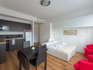 A modern, compact room with a kitchenette, a bed, a dining table, and a red chair. - Casa Sabotino Modern Functional and Cozy (Bologna)