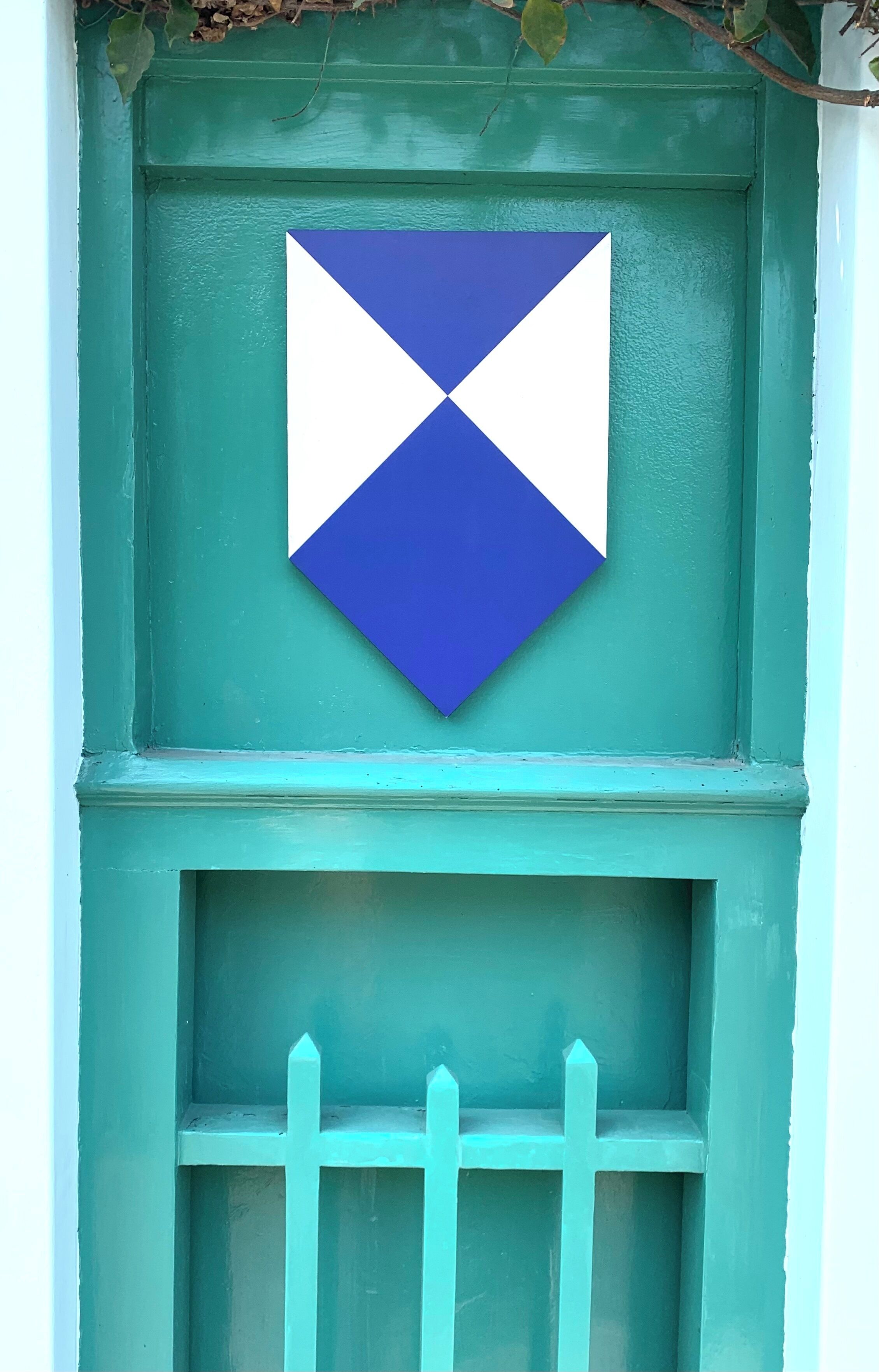 A teal door with a white and blue diamond-shaped sign.
