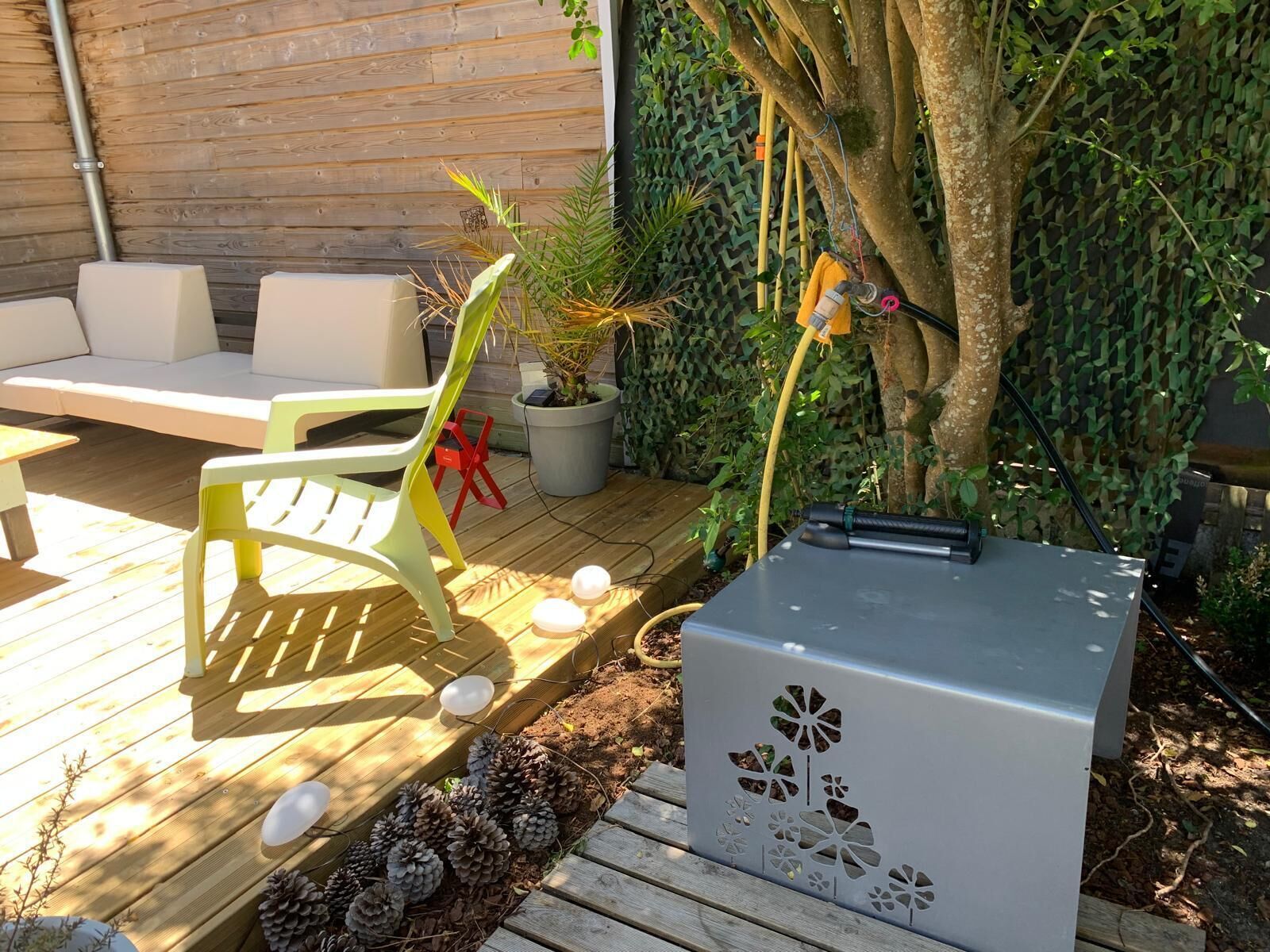 Een houten terras met buitenmeubilair, een plant in pot en een grijze technische kast.