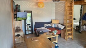 Un soggiorno accogliente con pavimento in legno, un divano con cuscini, un tavolino da caffè, una TV montata a parete e una scala appoggiata al muro.