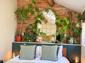 A bedroom with a brick wall, a large mirror, and various plants. - Luxury Rustic Barn Retreat in Llanrwst (Llanrwst)