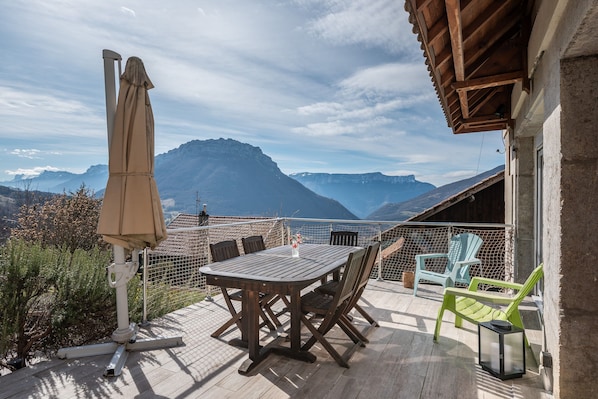 A wooden deck with a table and chairs, a hanging umbrella, and a view of mountains.