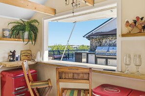 Une pièce avec une chaise en bois, un réfrigérateur rouge de style rétro et une fenêtre donnant sur une terrasse extérieure et un espace barbecue.