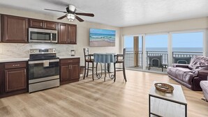 A modern kitchen with a microwave, oven, and dining area with a table and chairs. There is a balcony with a view of the ocean. - ☀️Oceanfront | Direct Beach Access | Two Pools | Daytona Inn Beach Resort 409☀️ (Daytona Beach)