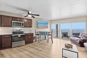 A modern kitchen with a microwave, oven, and dining area with a table and chairs. There is a balcony with a view of the ocean. - ☀️Oceanfront | Direct Beach Access | Two Pools | Daytona Inn Beach Resort 409☀️ (Daytona Beach)