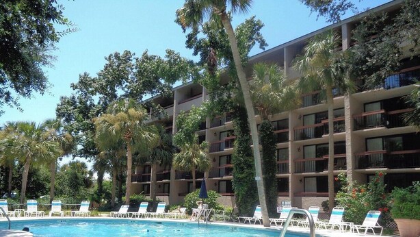 A hotel with a swimming pool surrounded by palm trees and lounge chairs.