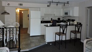 A compact kitchen with white cabinets, a central island, and a dining area with white chairs.