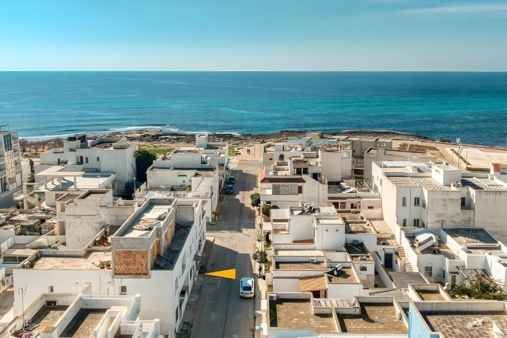 A coastal urban area with white buildings, a clear blue sky, and the sea in the background.