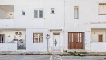 A white two-story residential building with a front door, a small balcony, and a no parking sign.