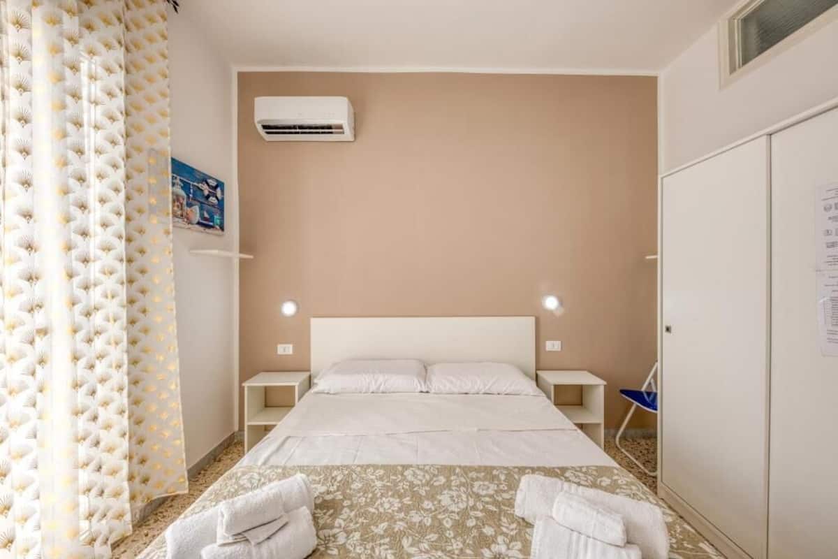A bedroom with a bed, bedside tables, an air conditioning unit, a wardrobe, and a shower curtain.