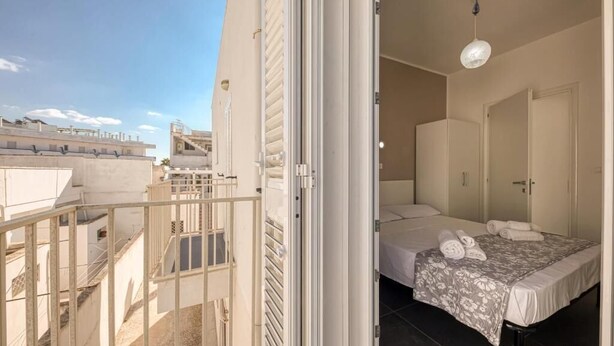 A hotel room with a balcony, a bed with a floral bedspread, and a hanging light fixture. - Il Comandante (Torre San Giovanni)