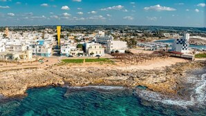 A coastal town with buildings along the shore, a rocky beach, and a clear view of the sea. - Il Comandante (Torre San Giovanni)