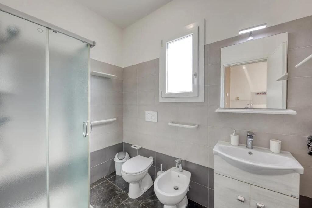 Un bagno moderno con cabina doccia in vetro, un water, un bidet, un lavandino e uno specchio.