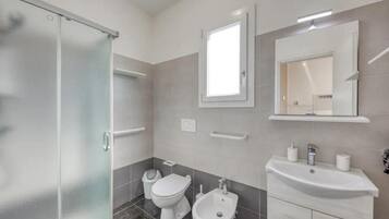Un bagno moderno con cabina doccia in vetro, un water, un bidet, un lavandino e uno specchio.