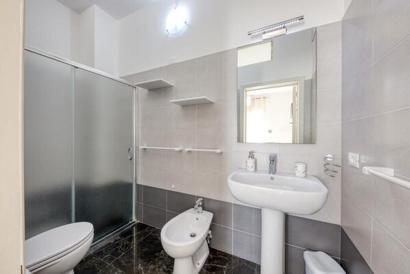 A modern bathroom with a toilet, bidet, and glass shower enclosure. - Il Comandante (Torre San Giovanni)
