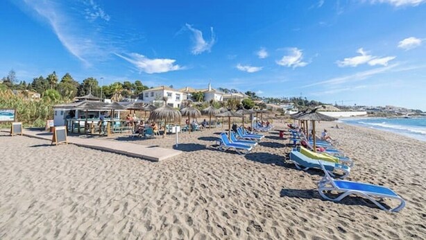 Een strand met ligbedden, parasols en een gebouw met een zwembad.