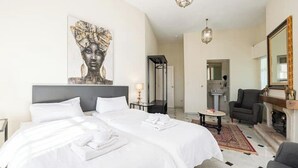 Een hotelkamer met twee bedden, een groot kunstwerk aan de muur, een open haard en een spiegel.