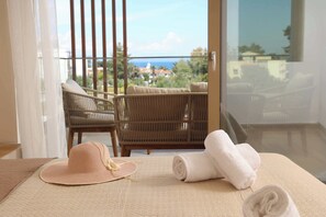 Una habitación con vista al océano, una silla de mimbre, una toalla enrollada y un sombrero de paja.