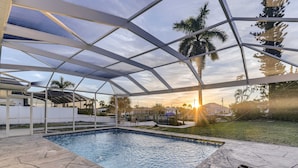 Una piscina exterior techada con vista a palmeras y una puesta de sol.
