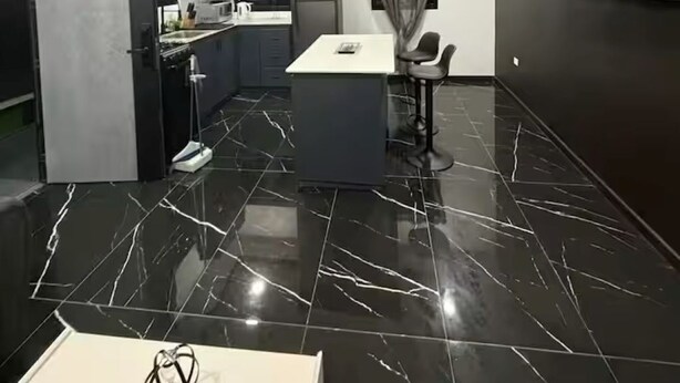 A modern kitchen with dark cabinetry, a central island, and a flat-screen TV mounted on the wall. - Storebay Suites - Apartment 5- (Tobago)