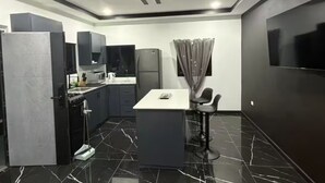 A modern kitchen with dark cabinetry, a marble countertop, and a bar area with stools. - Storebay Suites - Apartment 5- (Tobago)