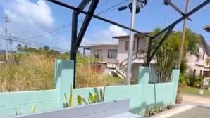 A modern outdoor seating area with a built-in fire pit, surrounded by a metal structure and a green wall. - Storebay Suites - Apartment 5- (Tobago)