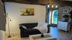 Ein Wohnzimmer mit einer schwarzen Couch, einem weißen Couchtisch, einem gewebten Ottomanen, einem Gemälde an der Wand und einer Steinwand mit einem Fenster.