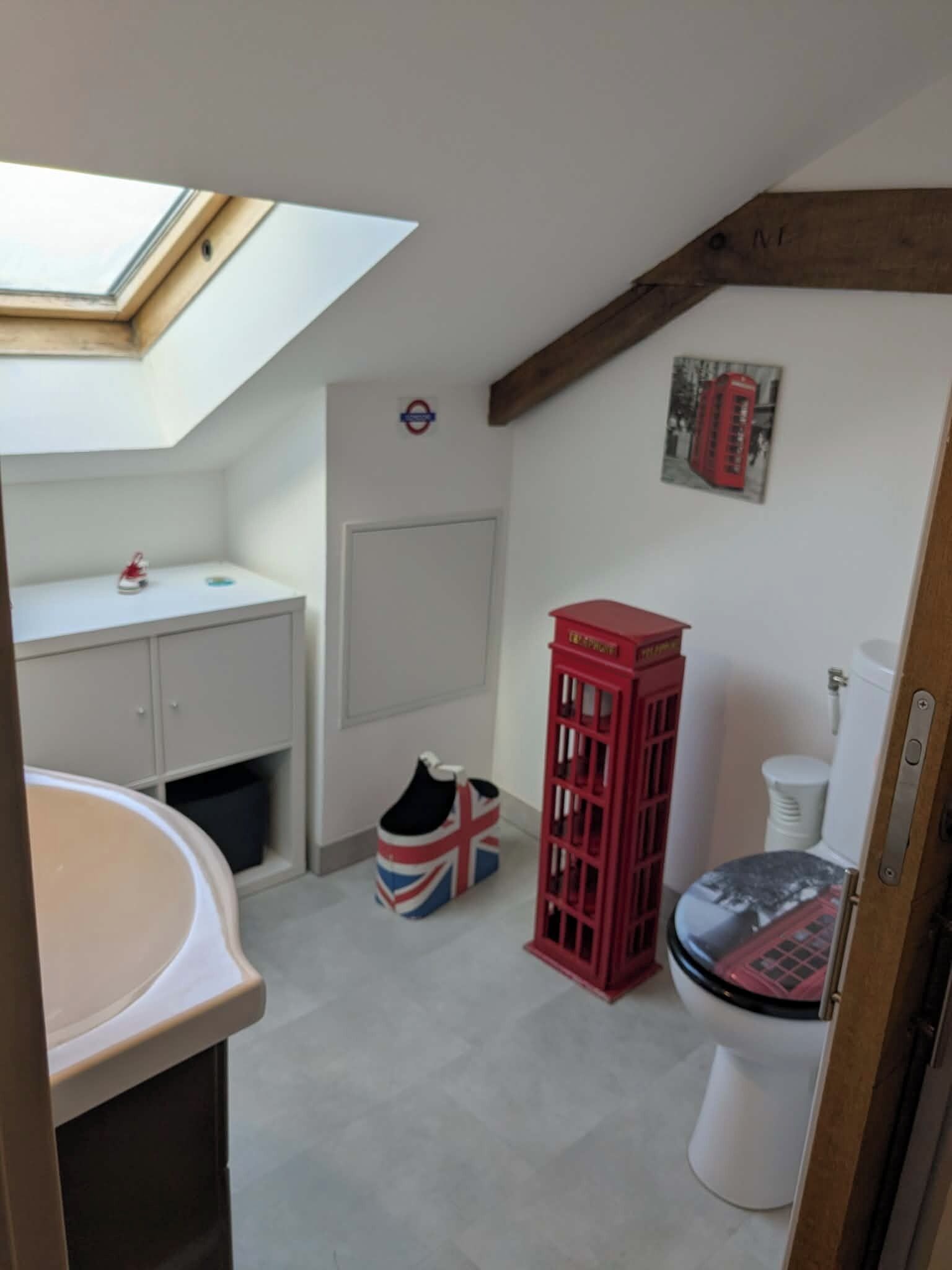 A compact bathroom with a skylight, a red telephone booth, and a Union Jack bag.