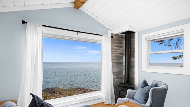 Quarto acolhedor com uma grande janela vista para o mar, lareira e área de estar com uma mesa.