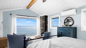 Quarto com uma cama grande, cômoda, cadeira e vista para o mar.