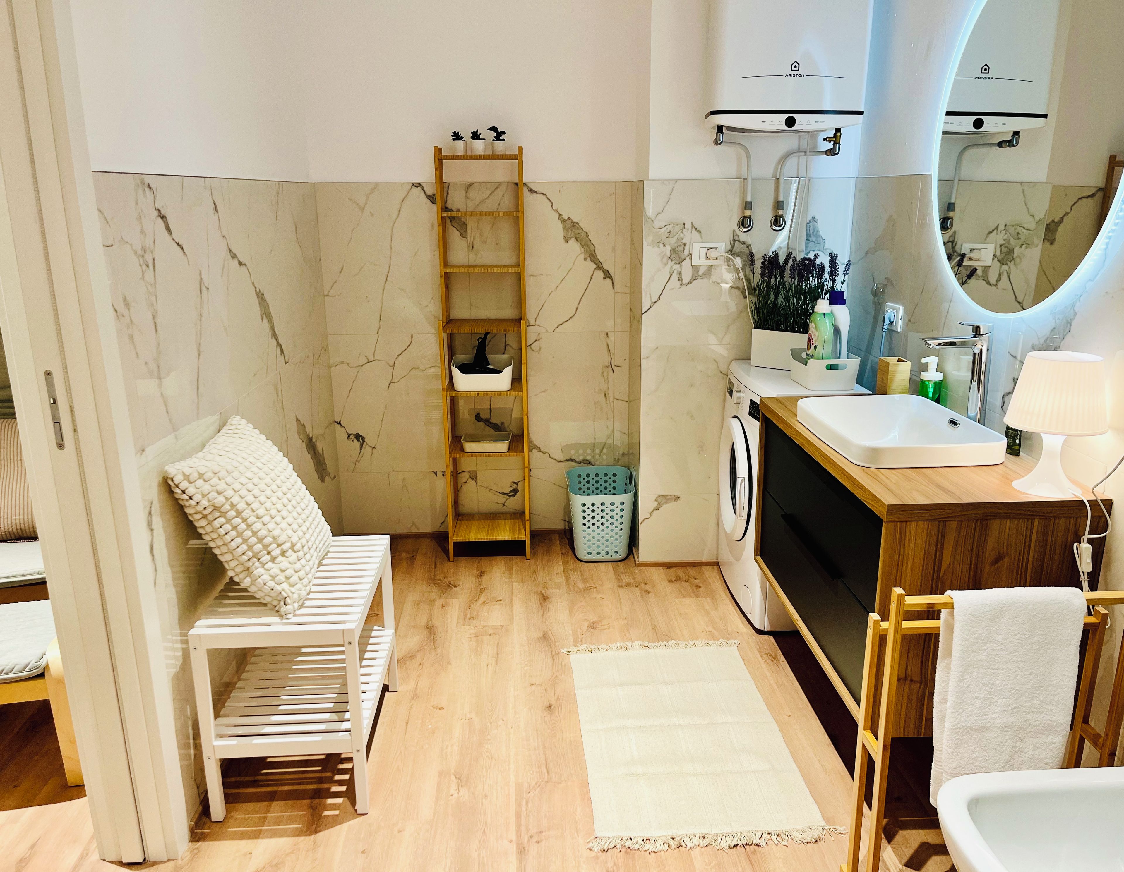 A bathroom with a wooden bench, a washing machine, a sink, a mirror, and a towel rack.