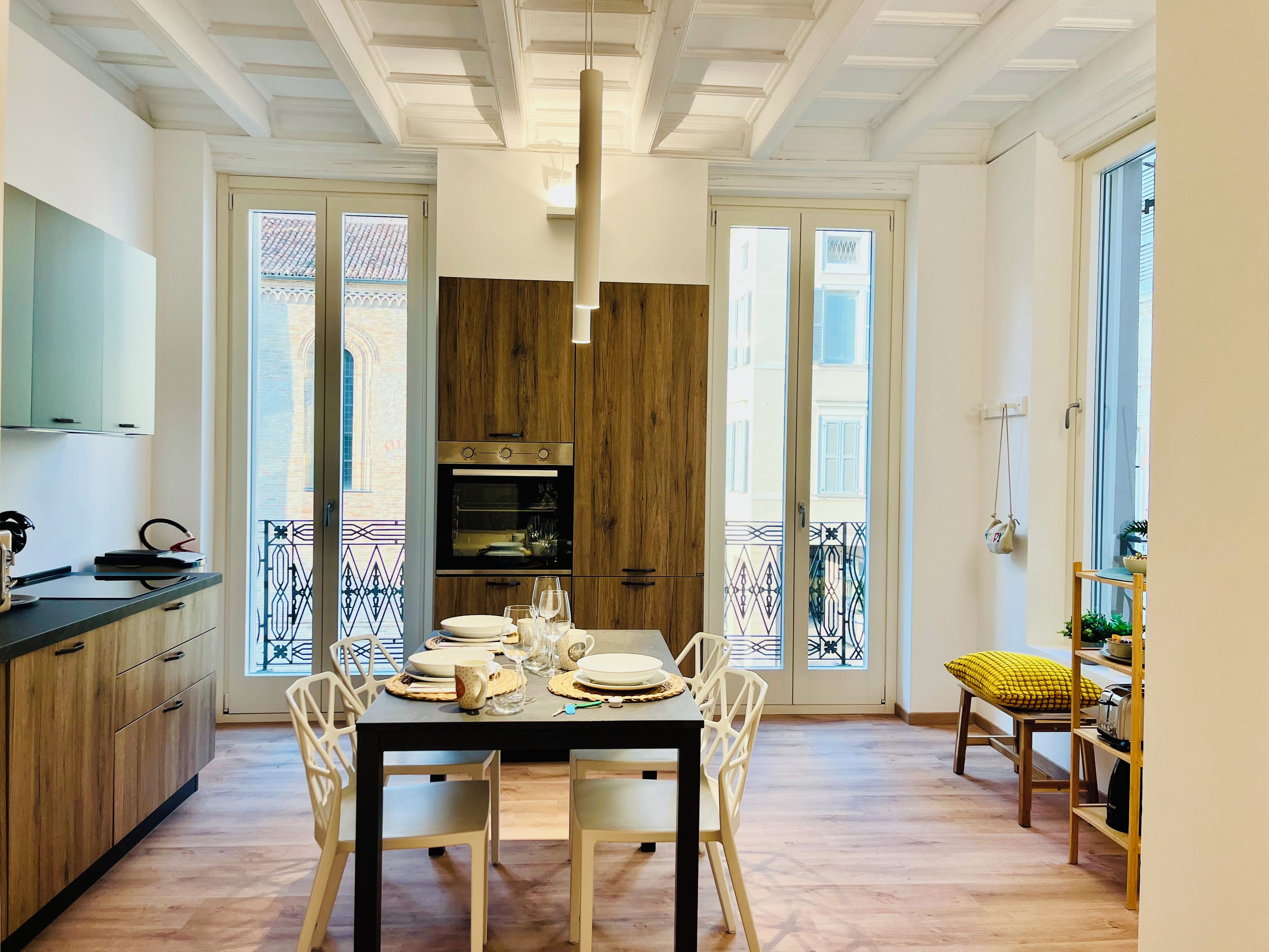 A dining area with a wooden table set for four, a kitchen with wooden cabinets, and a balcony with a railing.