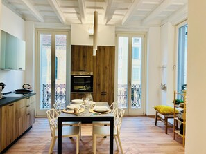 Un coin repas avec une table en bois dressée pour quatre personnes, une cuisine avec des placards en bois et un balcon doté d’une balustrade.