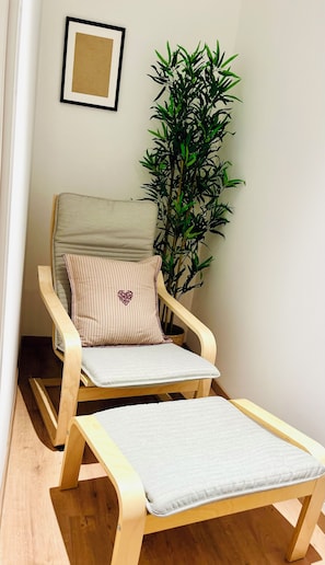 Ein Holzstuhl mit Kissen und ein kleiner Tisch, ein Blumentopf und ein gerahmtes Bild an der Wand.
