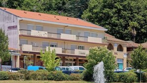 Un hotel con tetto in tegole rosse, diversi balconi e una fontana in primo piano.
