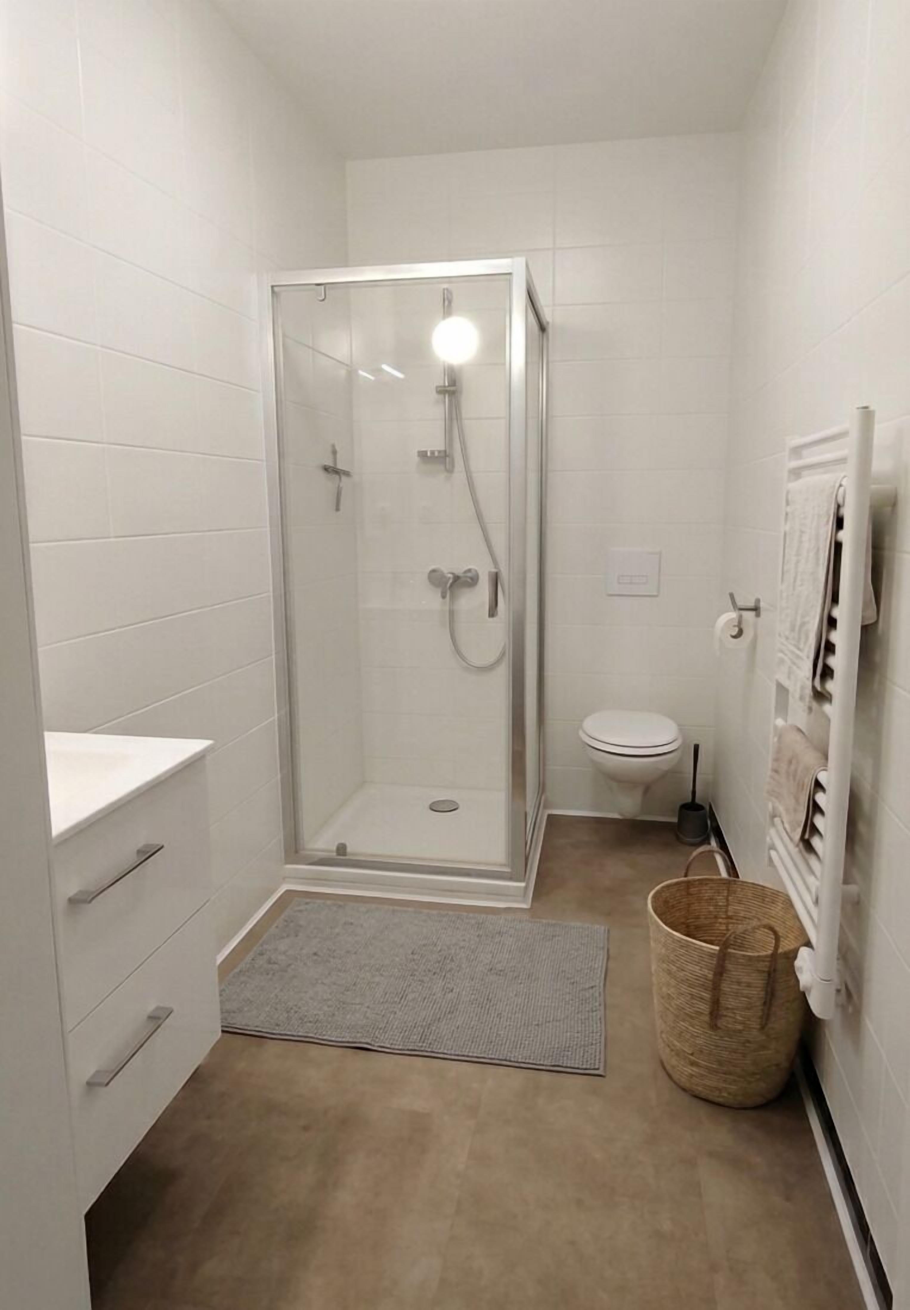 A small, modern bathroom with a glass-enclosed shower, a toilet, and a white sink.