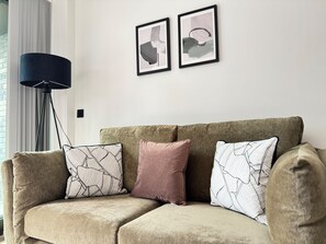 A beige sectional sofa with patterned cushions, a black floor lamp, and abstract artwork on the wall. - Stylish 2-Bed Apartment - Balcony - Parking (Manchester)