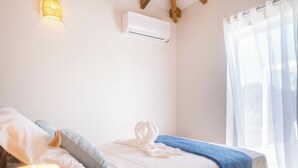 Ein Schlafzimmer mit einem Bett, einer Wand-Klimaanlage, einer Nachttischlampe und einem Fenster mit transparenten Vorhängen.